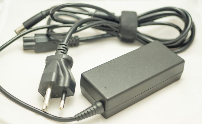 A computer adapter in black color with a circut box and plug on a white background.